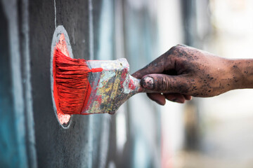A closeup shot of a graffiti artist's hand dirty in paint holding a paintbrush and painting on a...