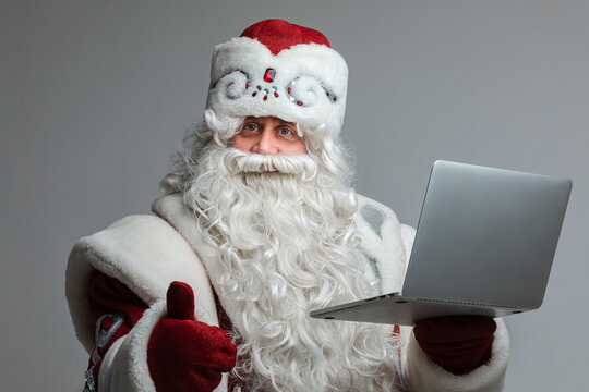 father frost with long beard do something with a laptop and looks to the camera, picture isolated on grey background