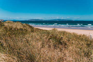 Fototapeta na wymiar pristine wild landscape at Clifton Beach in Tasmania, Australia with wavy blue ocean and golden sand next to a rugged coastline