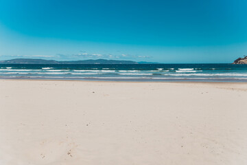 pristine wild landscape at Clifton Beach in Tasmania, Australia with wavy blue ocean and golden sand next to a rugged coastline