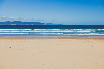 pristine wild landscape at Clifton Beach in Tasmania, Australia with wavy blue ocean and golden sand next to a rugged coastline