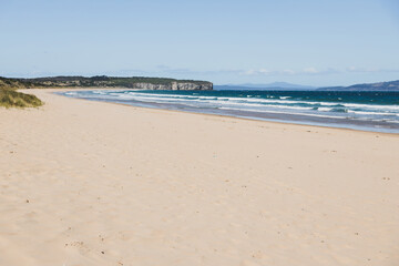 pristine wild landscape at Clifton Beach in Tasmania, Australia with wavy blue ocean and golden sand next to a rugged coastline
