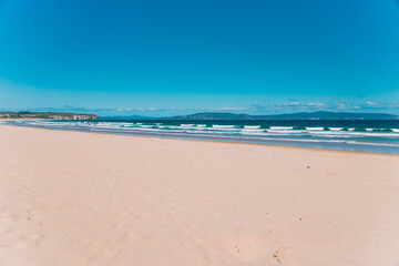 pristine wild landscape at Clifton Beach in Tasmania, Australia with wavy blue ocean and golden sand next to a rugged coastline