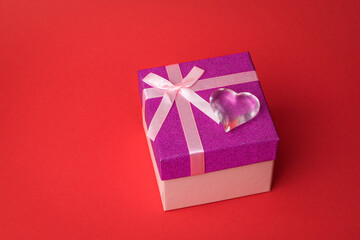 Glass heart on a gift box on a red background.