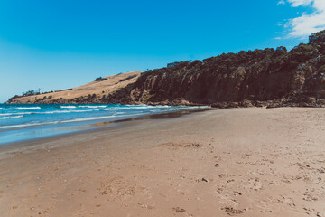 pristine wild landscape at Clifton Beach in Tasmania, Australia with wavy blue ocean and golden sand next to a rugged coastline