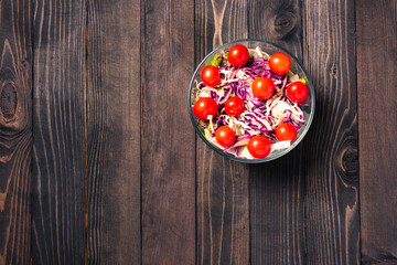 Top view of the healthy colorful salad bowl with tomatoes fresh mixed greens vegetable in a dish on black wooden background, Health salad snack food concept