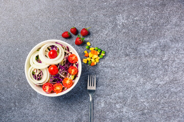 Top view of the healthy colorful salad bowl with tomatoes fresh mixed leaves vegetable in a dish on cement stone table background, Health salad snack diet food weight loss concept