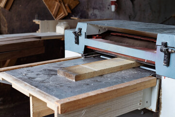 Carpenter working automated sanding machine for wood boards.