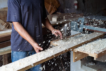 Carpenter working automated sanding machine for wood boards.