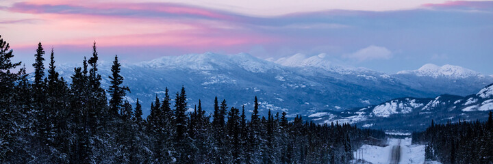 Panoramic view of the Yukon Territory, northern Canada in wintertime sunrise over snow capped mountains, woods, forest and wilderness with pink and blue tones. 