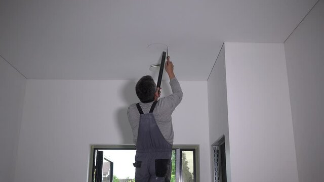Worker man saw hole for round led panel in plasterboard ceiling