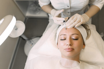 doctor cosmetologist makes an injection of medicine in the forehead of a woman patient