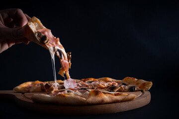 A closeup of a person taking a slice from a freshly baked pizza with ham and mushrooms