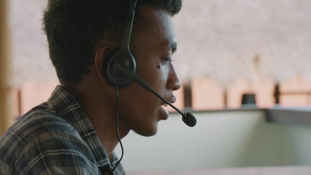 Close up of young Asian man wearing checkered shirt and headphones consulting client by phoneClose up of young Asian man wearing checkered shirt and headphones consulting client by phoneClose up of yo