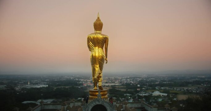 Girl walks close to golden buddha statue with citycape view late evening