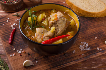 Deep plate with stewed potatoes and chicken meat on a wooden table
