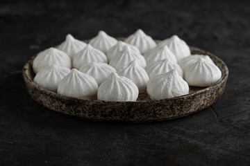 White sweet meringue in ceramic round bowl and plate on concrete background.