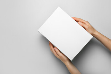 Hands with blank cardboard box on light background