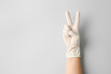 Hand in protective glove showing victory gesture on light background