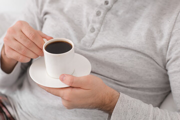 Morning of young man drinking hot coffee in bed, closeup