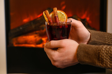 Woman with glass of tasty mulled wine near fireplace