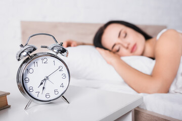 classic alarm clock and blurred young woman sleeping in bed on background