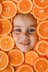 The face of a beautiful little girl is surrounded by pieces of sliced orange, orange useful fruit rich in vitamin C.
