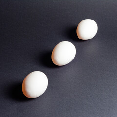 Three white eggs on a black background, dietary and healthy food rich in protein.