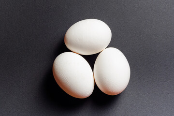 Eggs on a black background, three eggs in a row, shadow on the background of eggs, healthy and diet food.