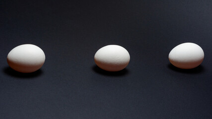 Eggs on a black background, three eggs in a row, shadow on the background of eggs, healthy and diet food.