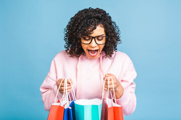 Sale concept! Beautiful black african american woman smiling and holding shopping bags isolated over blue background.