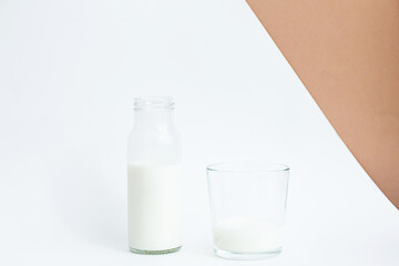 Minimalist still life of milk bottle and glass cup on white and beige background. The concept of ecological and healthy and lifestyle