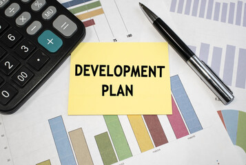 On a document with a color chart near the calculator is a yellow sheet on which the word development plan is written. Business concept
