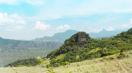 Single rock peak covered by trees and bushes with a background mountain range.