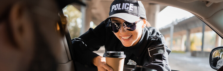 happy policewoman with paper car looking at african american colleague in patrol car on blurred foreground, banner. © LIGHTFIELD STUDIOS