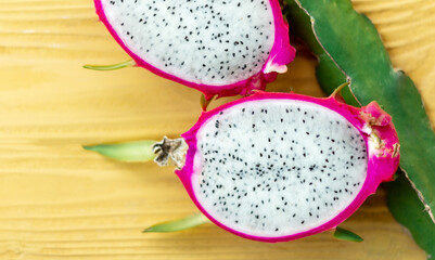 half cuted dragon fruit and branch on yellow wooden background. Healthy food, diet, menu, tropical fruit, summer concept. Top view