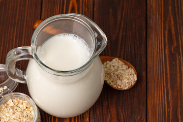 Glass pitcher of milk and oat flakes on wooden table