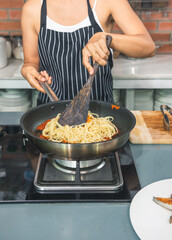 Women chef cooking spaghetti  tomato sauce with pan on gas stove in the kitchen. Female Cooking Italian pasta with creamy red sauce. Cooking food concept. 