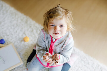 Sad crying toddler girl learning painting with felt tip pens. Little baby child drawing on hands and clothes. Angry child in hysteric crisis as parents scold with daughter for dirty hands.