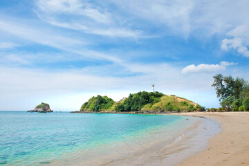 Fototapeta na wymiar Beautiful seascape with a tropical beach. Against the background of a blue cloudy sky, a green hill with a white lighthouse. Koh Lanta, Thailand