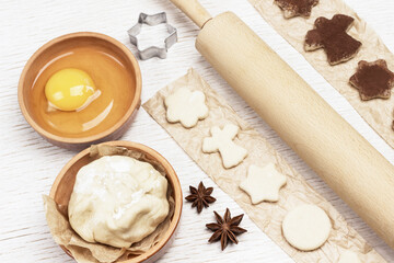 Cutting shaped cookies by mold sprinkled with chocolate on paper. Eggs, Dough, cinnamon sticks and rolling pin