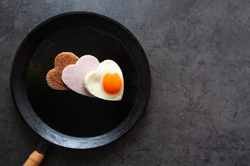 pan with fried egg, bread and ham in shape of heart on dark grey background, valentine's day concept,  top view