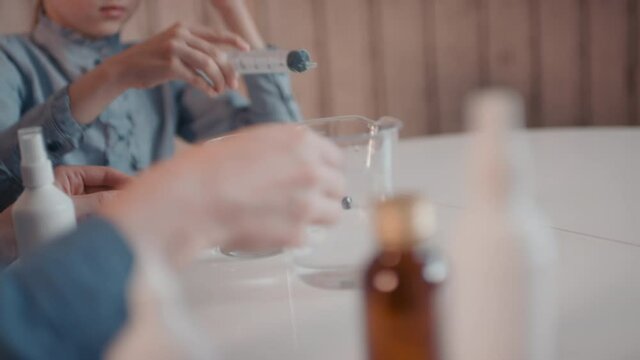 Slow-motion close-up of unrecognizable little girl making sanitizer at home adding hydrogen peroxide to measuring cup using syringe