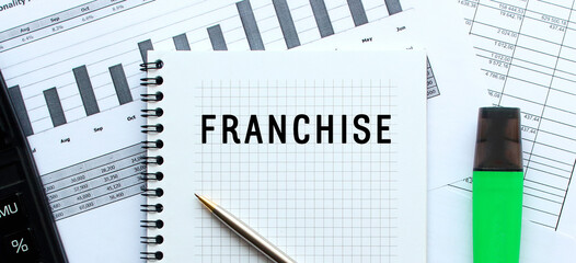 Text FRANCHISE on the page of a notepad lying on financial charts on the office desk.