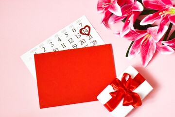 Valentine's day postcard. Calendar, gift box, lily flower and red paper for text on a pink background. concept of holidays Valentine's Day.
Copy space, flat lay.