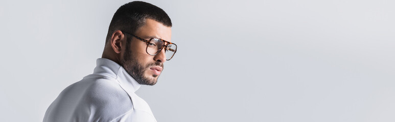 Obraz premium Bearded man in eyeglasses and white turtleneck looking away isolated on grey, banner