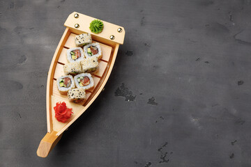 Sushi roll served on wooden boat plate on black background