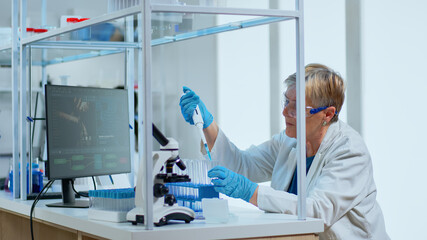 Senior scientist woman pipetting liquid to test tube in modern equipped lab. Multiethnic team...