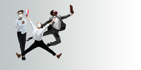 Happy office workers in face masks jumping and dancing in casual clothes or suit isolated on studio background. Business, start-up, prevention of COVID, motion and action concept. Creative collage.