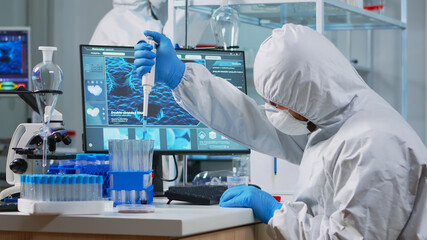 Scientist man pipetting liquid to test tube wearing protection suit in lab. Team of doctors...